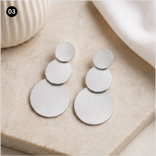 Boucles d’oreilles argentées à trois disques NIRMEN présentées sur tissu